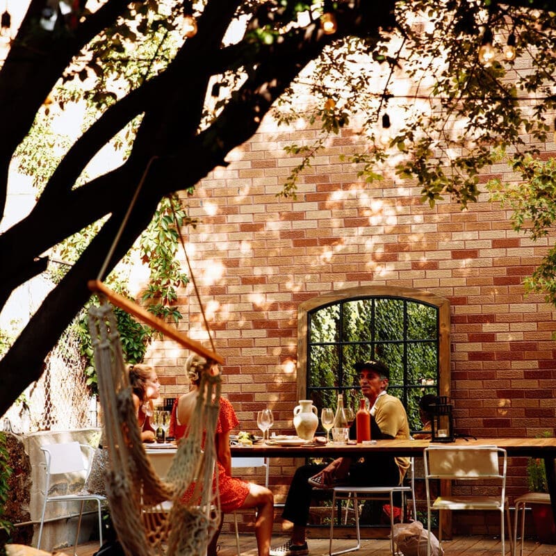 People sitting in sun dappled backyard drinking wine and talking at Sauced, a wine bar in New York City, NYC