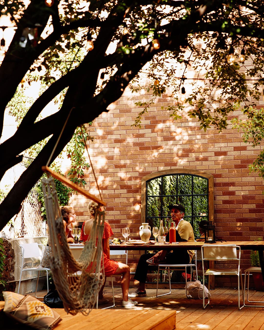 People sitting in sun dappled backyard drinking wine and talking at Sauced, a wine bar in New York City, NYC