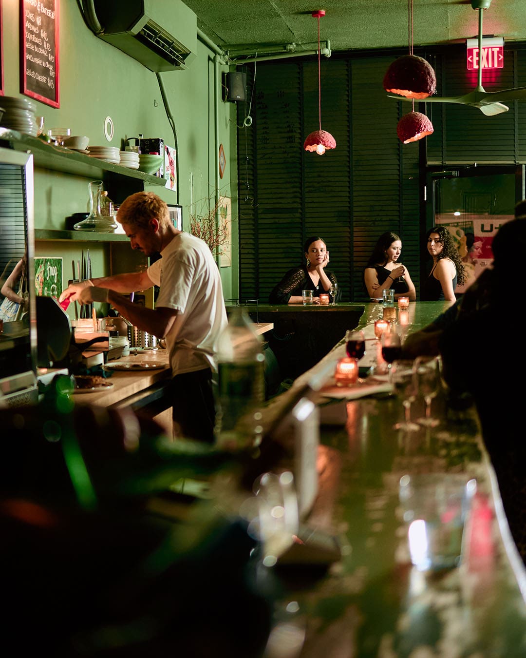 Bartender at Frog serves up natural wine surrounded by people at long central bar area, NYC