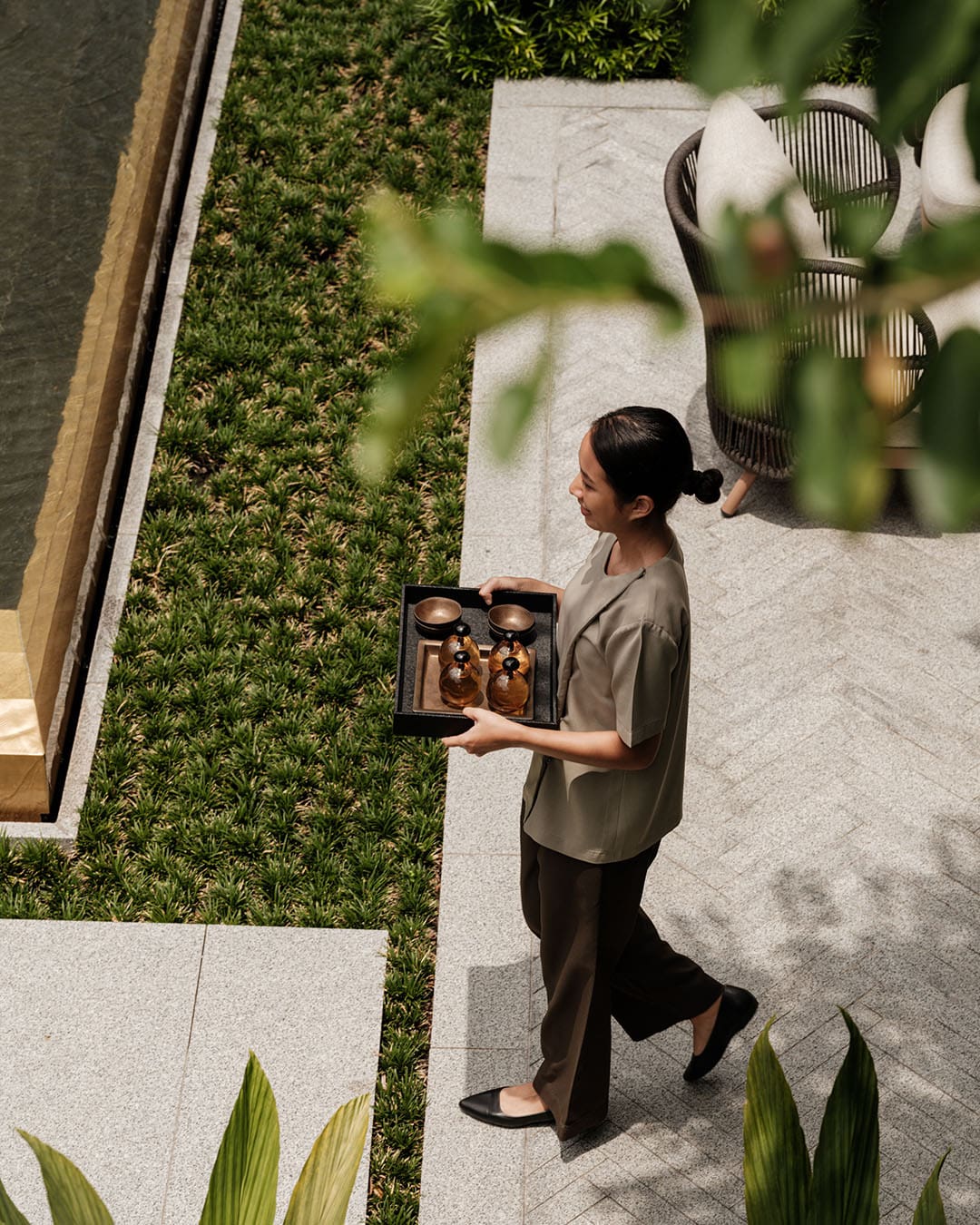 A woman carries a tray in the spa garden at Capella Bangkok