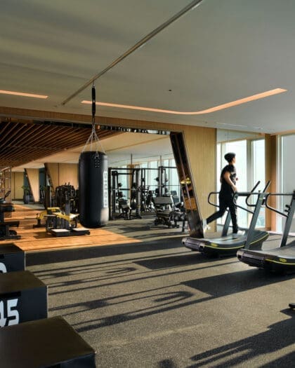 A man exercising on a running machine demonstrating hotel fitness at the Grande Lumphini hotel in Bangkok. Natural light streams in through the windows onto a vast array of exercise machines