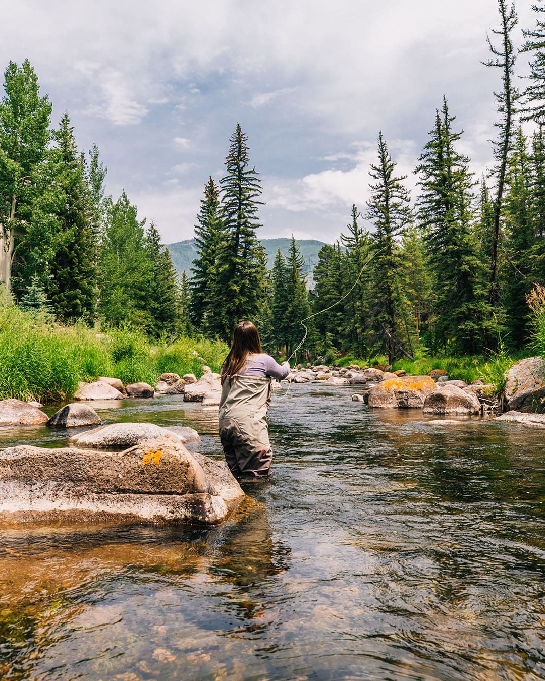 A woman enjoys fly fishing at the Grand Hyatt Vail in a picturesque setting