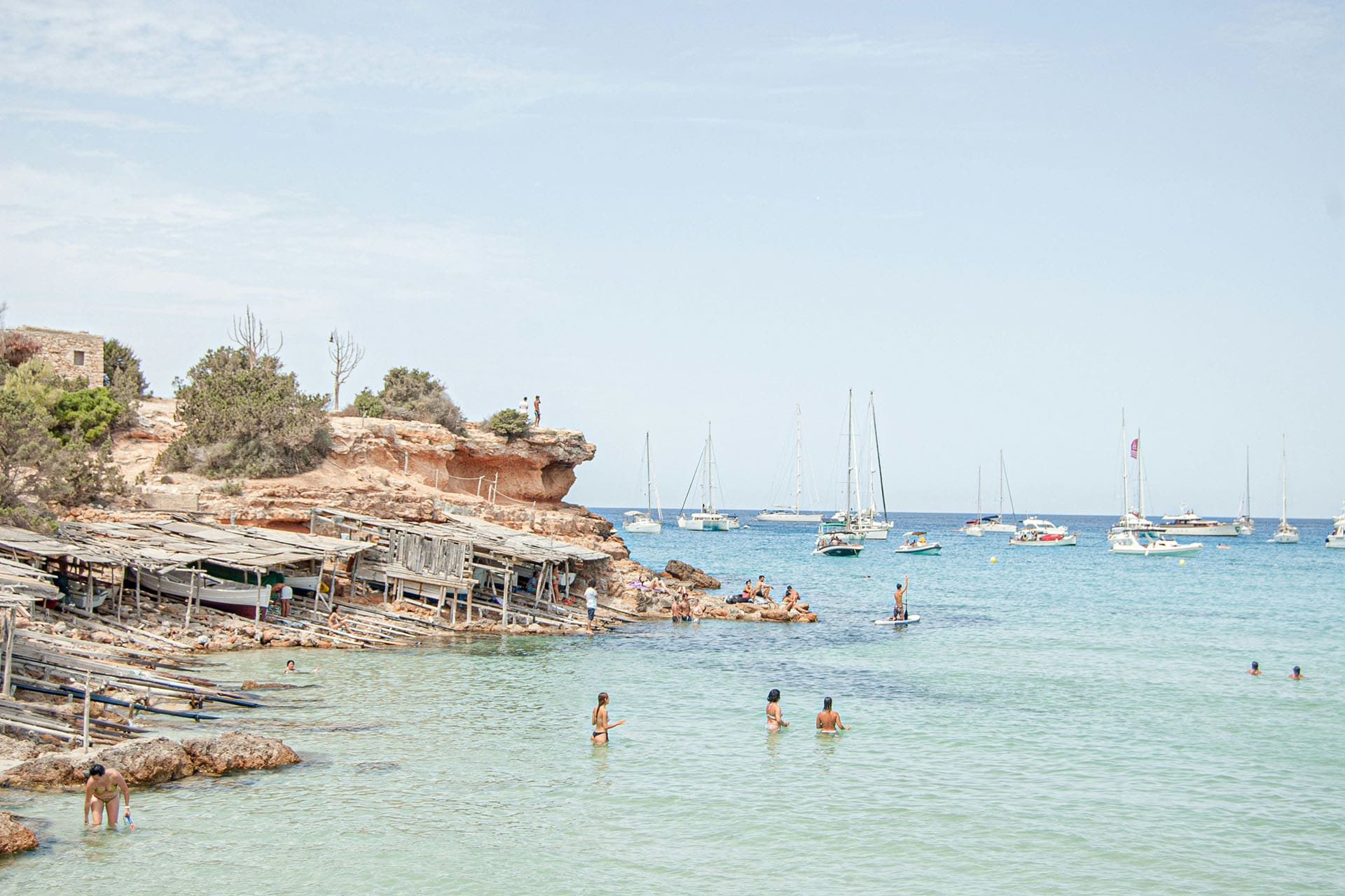 A beach scene in Formentera, tourists and swimmers enjoy the coastline with boats in background