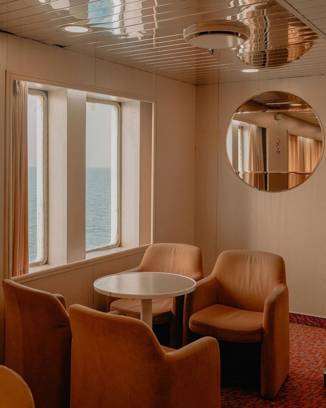 A ferry interior showing four lounge chairs and a round table next to a rectangular sea view window
