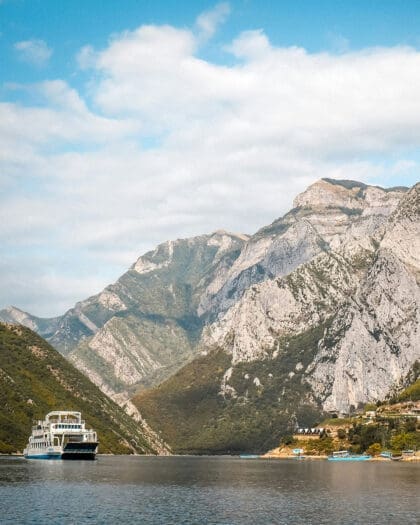 A ferry crosses Lake Komani in a mountainous landscape