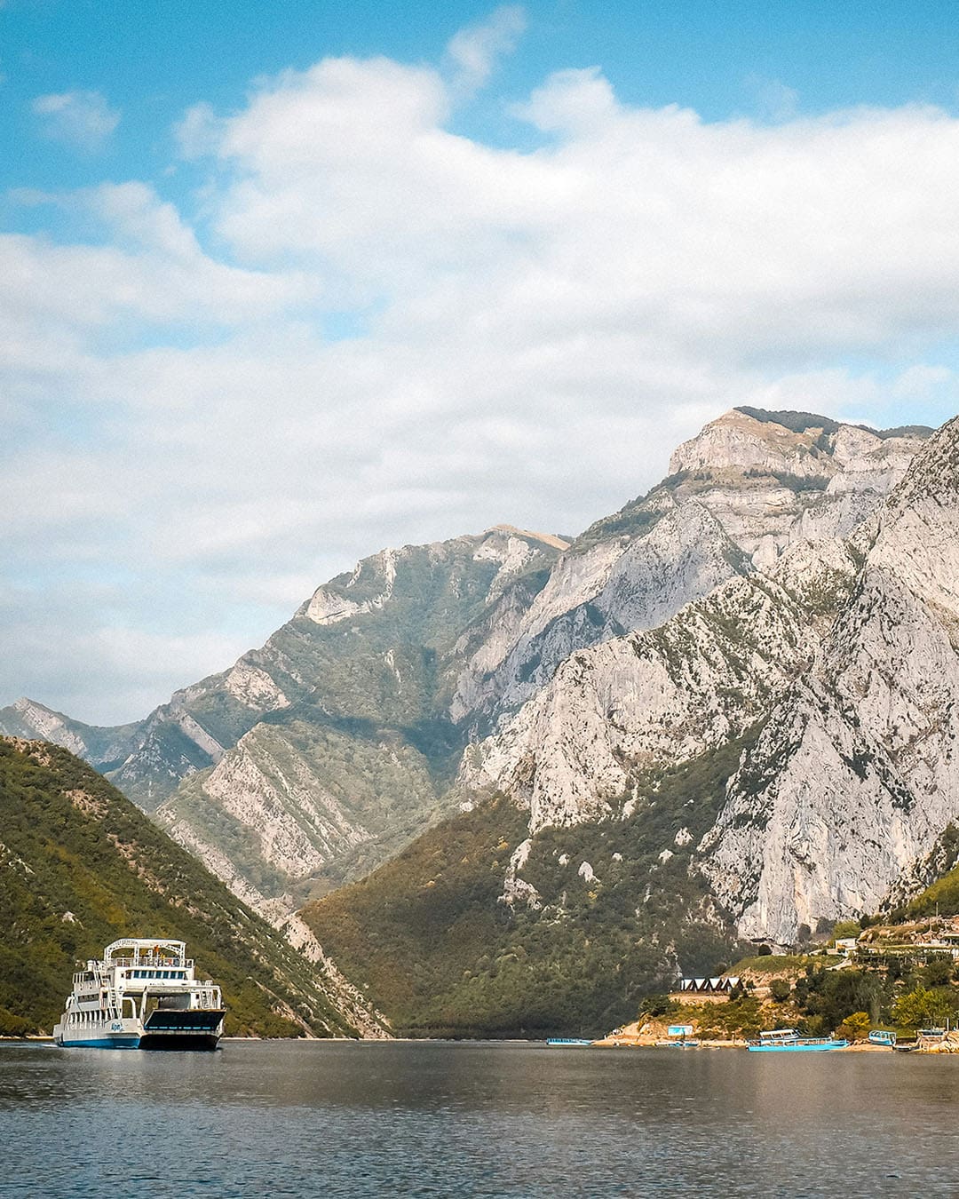 A ferry crosses Lake Komani in a mountainous landscape