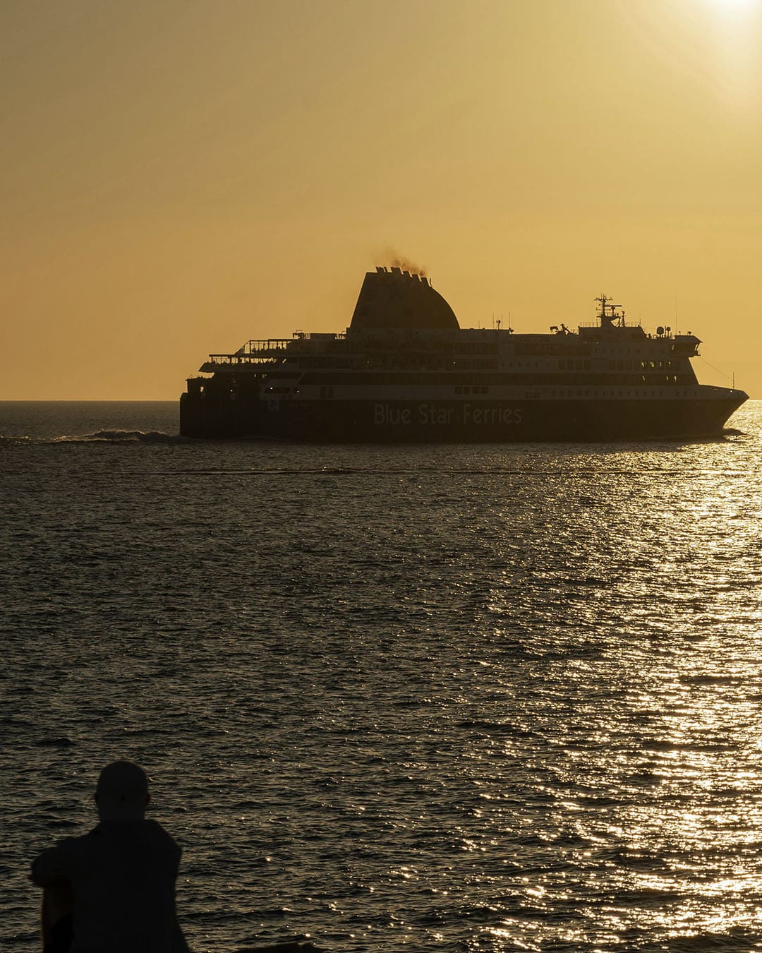 A blue star ferry at sunset with a person in the foreground