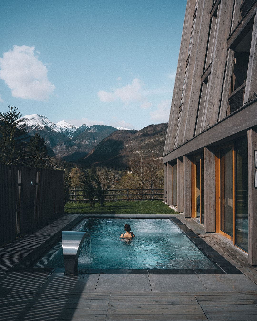A guest swims in the outdoor pool at Hotel Bohinj with mountains in background