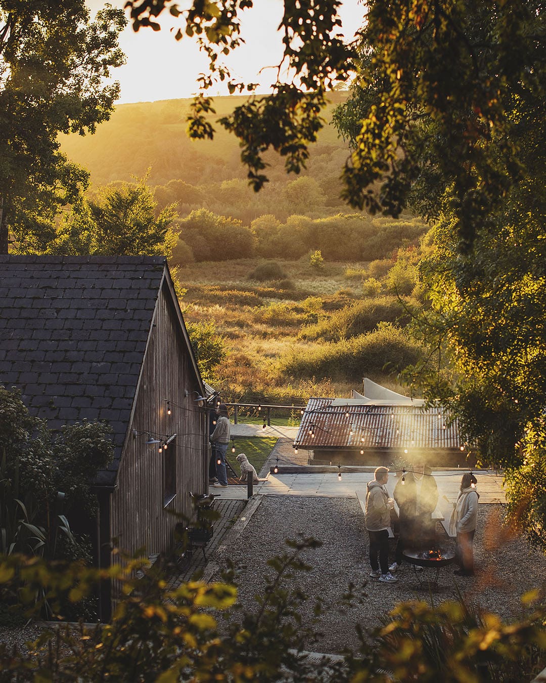 People standing around an open fire in a beautiful countryside surrounds and venue of fforest on Wales' coast