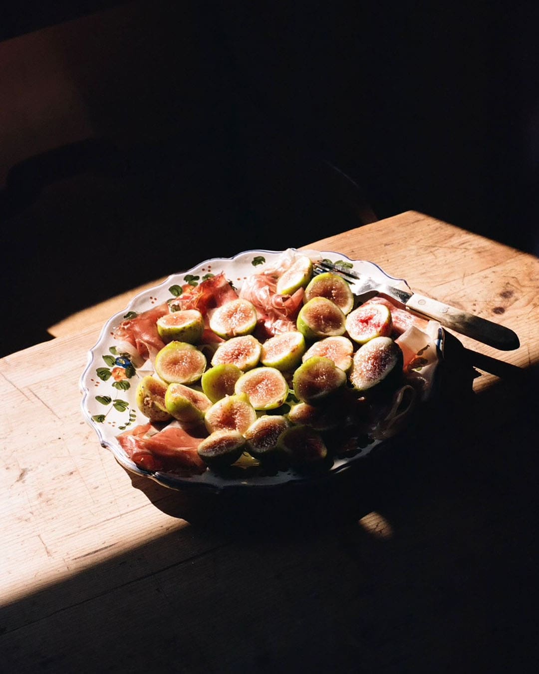Figs in a dish on a wooden table, sunlight falls in a stripe on the dish leaving half of it in shadow