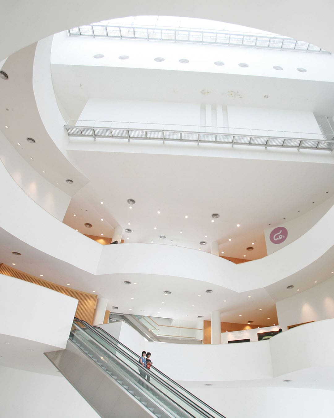 Two visitors ricicde the escalators of Bangkok Art and Culture Centre (BACC) in an organic circular architecture