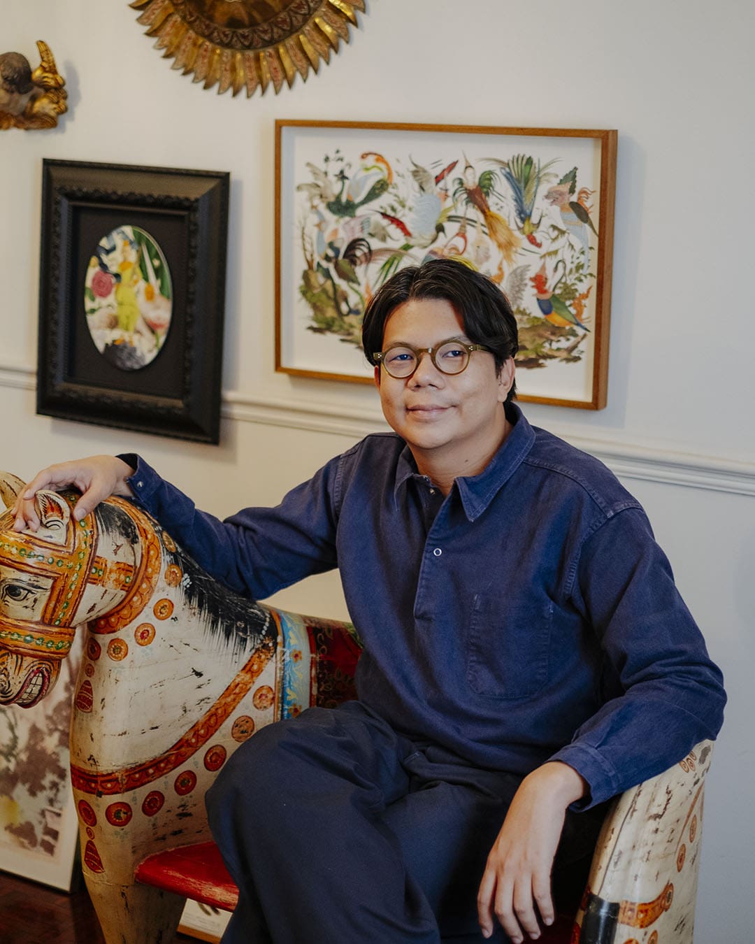 Artist Nakrob in his studio, sitting on an antique horse seat. Photography by Adam Birkan