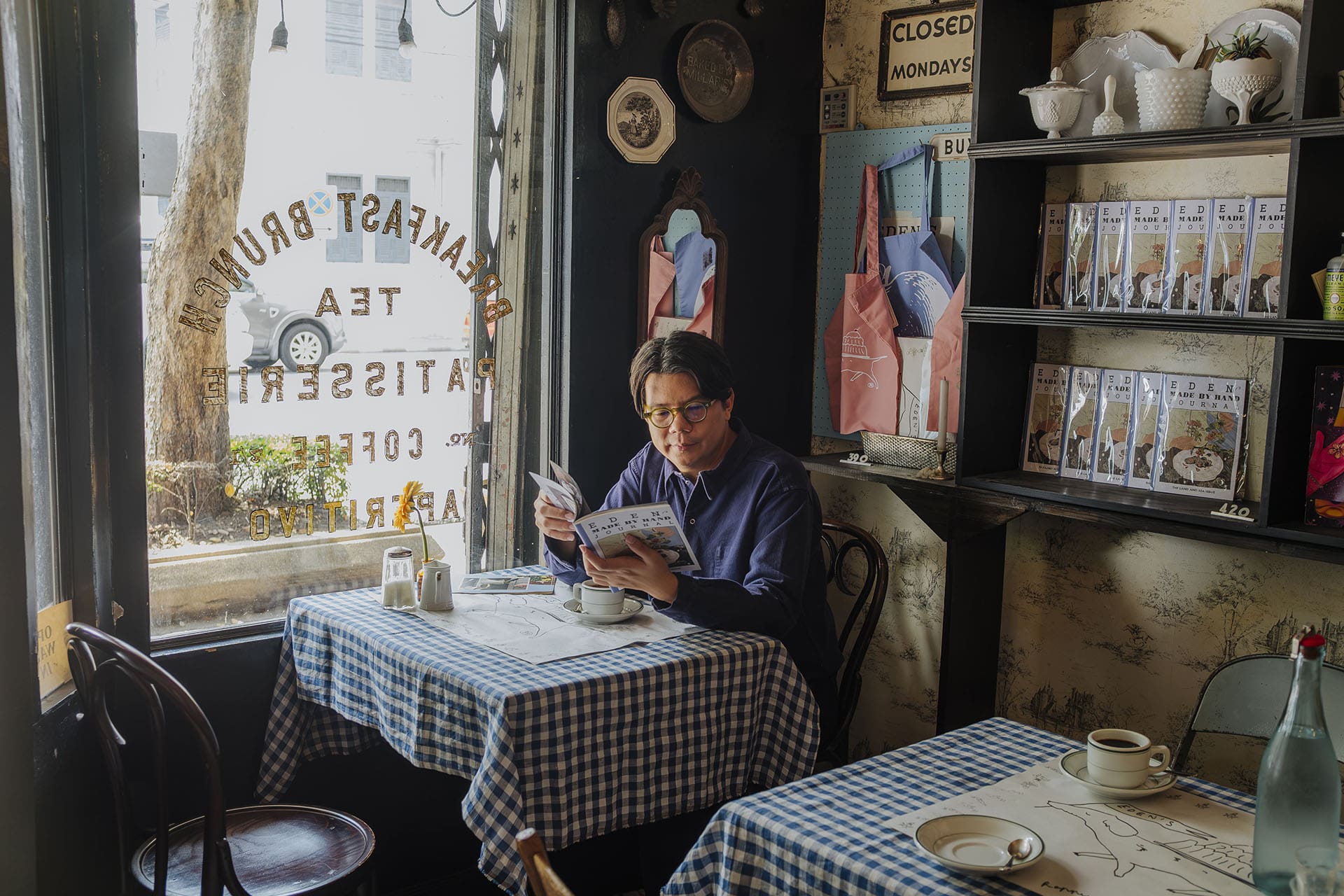 The artist, Nakrob Moonmanas sits in Eden's Cafe in Bangkok's Old Town. Surrounded by quirky items. Photography by Adam Birkan