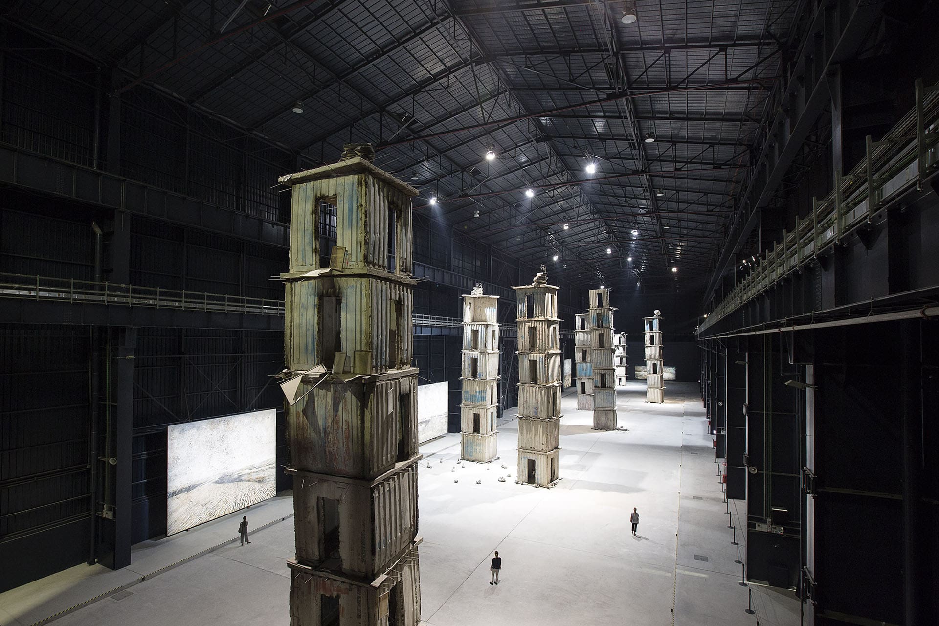 People walk between massive art installations inside a large aircraft hangar