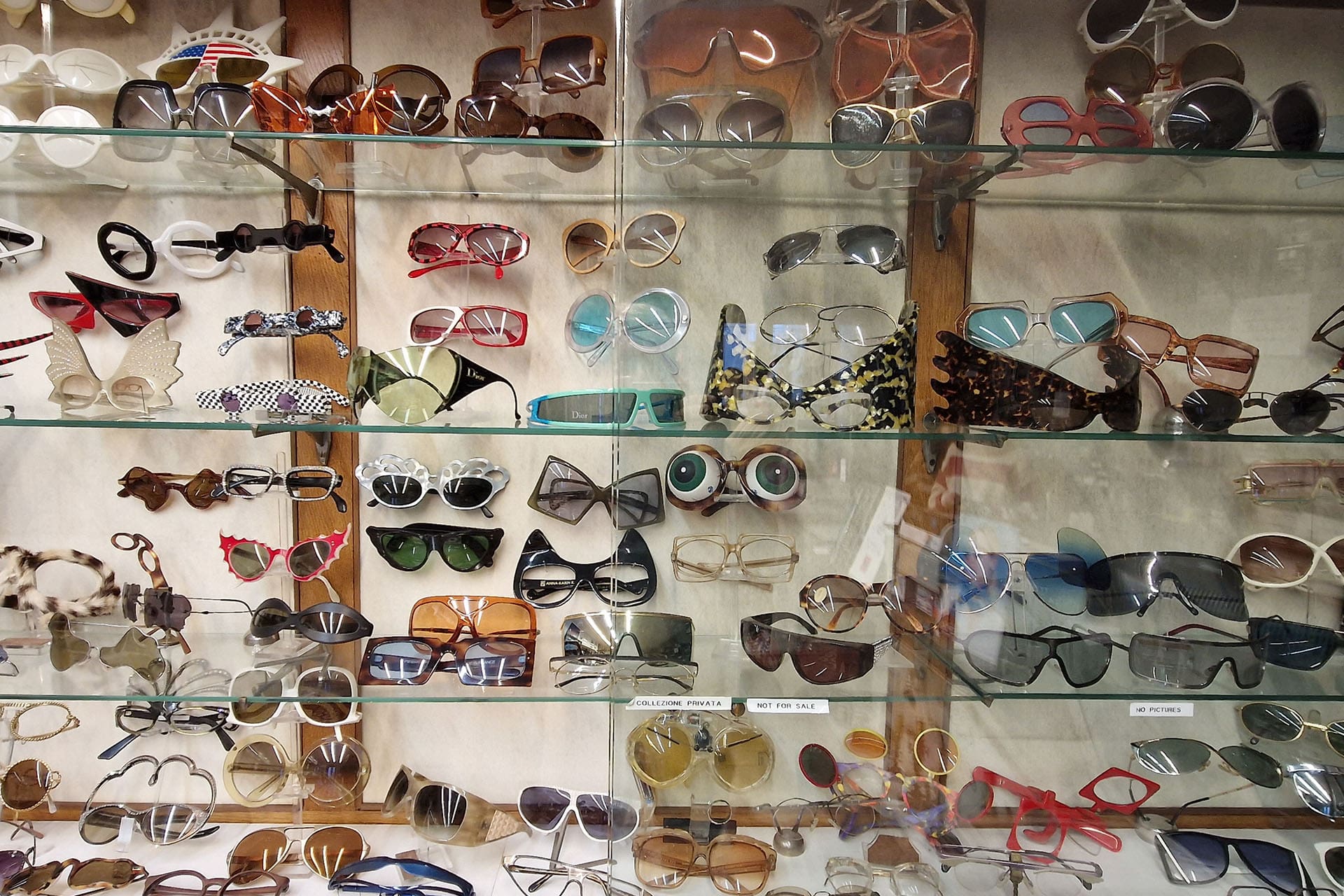 A large diverse selection of vintage glasses and sunglasses in a glass cabinet