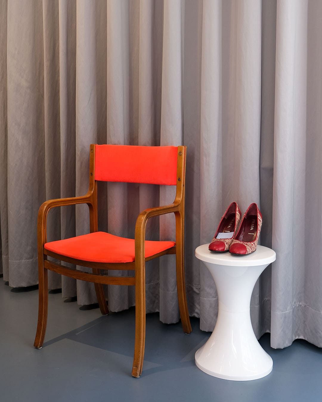 A red chair and a pair of designer high heels with a curtain background at Shop the Story