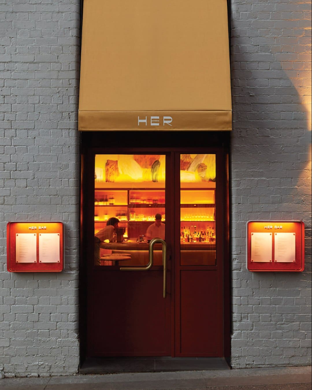 The exterior of HER in Melbourne with an orange glow within