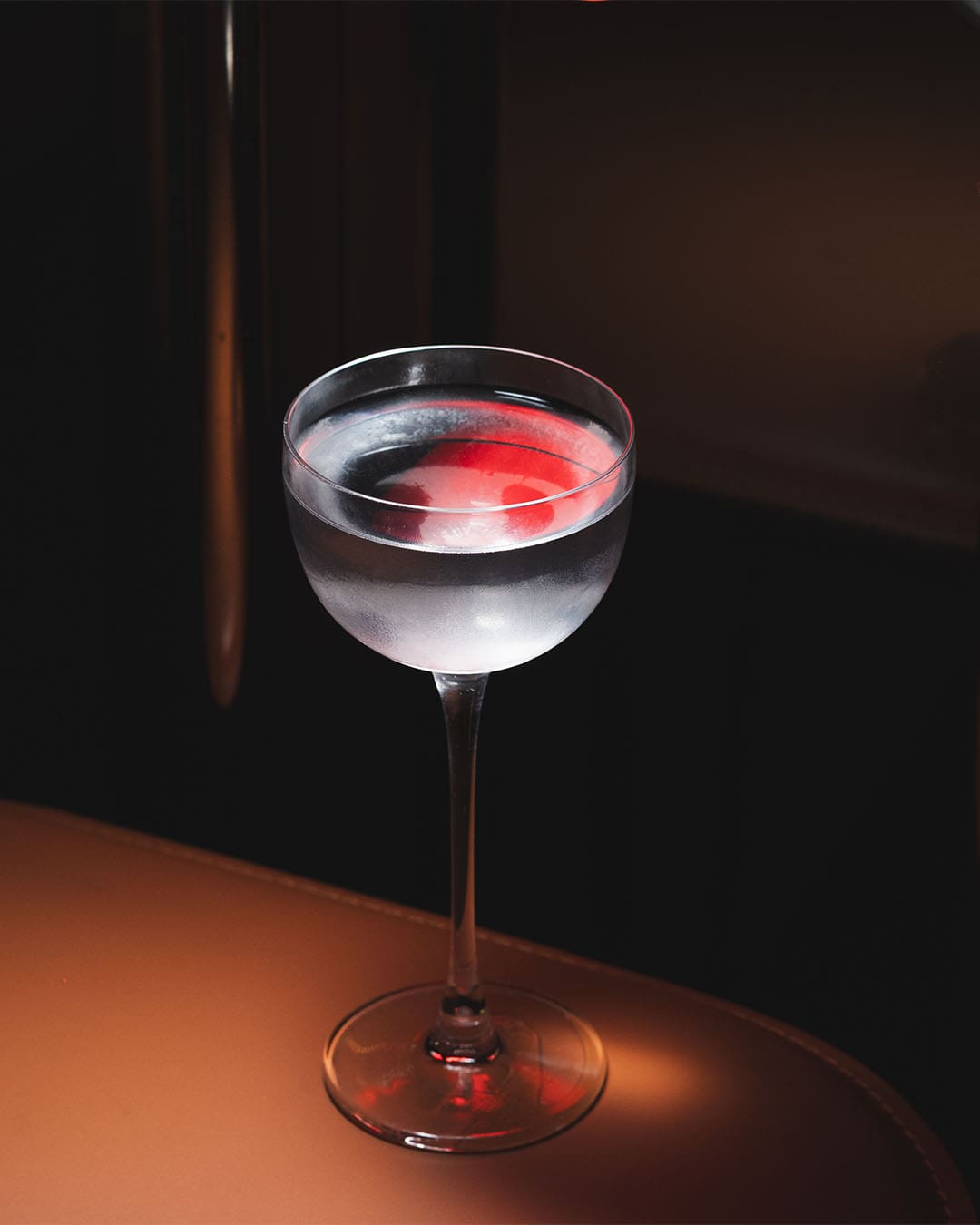 A clear cocktail with a red glow on top at BoB in Milan